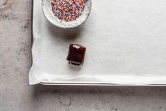 a bowl of sprinkles next to a plate with a piece of chocolate on it