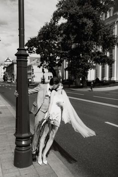 black and white photograph of a couple kissing on the sidewalk next to a street light