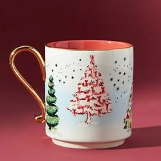 a coffee cup with christmas trees painted on it and gold trimming around the edge