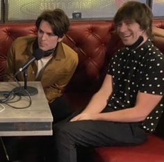 two people sitting on a red couch in front of a table with a microphone and headphones