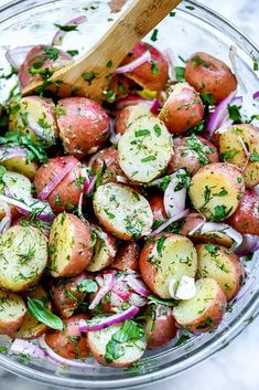 a glass bowl filled with red potatoes, onions and parsley next to a wooden spoon