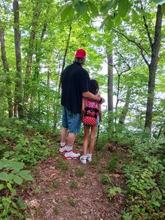 a man and child standing on a trail in the woods looking out at water from behind them