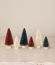 five small christmas trees are lined up in different colors and sizes, with one red white and the other blue