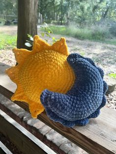 two crocheted sunflowers sitting on top of a wooden bench in the woods