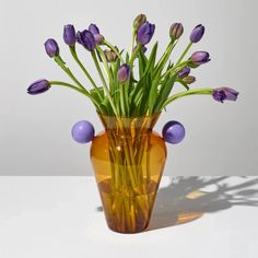 a vase filled with purple flowers sitting on top of a white table next to a shadow