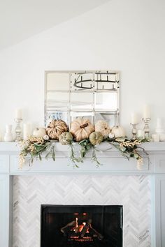 a white fireplace with pumpkins and greenery on top