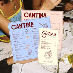 two menus sitting on top of a table with people eating food and drinking wine