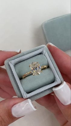 a woman's hand holding an engagement ring in a box