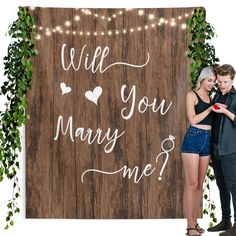 a man and woman standing next to a wooden sign that says will you marry me?