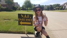 a young woman sitting on top of a sign giving the peace sign