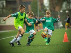 three young boys playing soccer on a field with people watching from the sidelines behind them