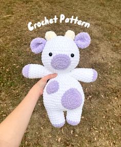 a hand holding a white and purple crocheted stuffed animal on grass with the words crochet pattern above it