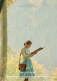 a woman in a blue dress is holding a book and looking at the ground with trees behind her