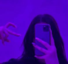 a woman taking a selfie with her cell phone in front of purple light and pointing at the camera