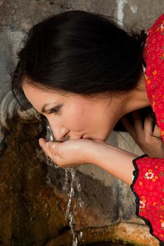 a woman in a red dress is drinking water from a fountain with her hands on her face