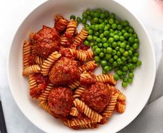 a white bowl filled with pasta and meatballs next to peas on top of a table