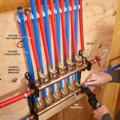 a man is working on an electrical wiring box with red and blue pipes attached to it