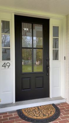 a black front door with two sidelights and a welcome mat on the brick walkway