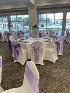 a banquet room set up with purple and white linens on the tables, chairs, and centerpieces