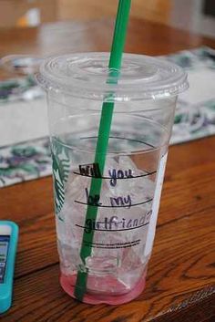 a plastic cup sitting on top of a wooden table next to a cell phone and paper