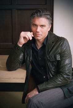 a man is sitting on a bench wearing a leather jacket and black shirt with his hand under his chin