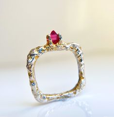 a gold and silver ring with a red stone on it's center, sitting on a white surface