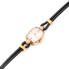 A vintage yellow gold watch, with champagne dial, 18 karat yellow gold watch case, and black leather strap with yellow metal fittings.  This elegant vintage cocktail watch is lozenge shaped and crafted in yellow gold. The gold has a soft, slightly rosy hue, and is complete with a champagne dial. The dial sports hour markers by way of dots and batons and has grooved loops at the top and bottom of the watch case, to which the strap is fastened. The black leather cord watch strap is a later replace Retro Black Watch Accessories For Formal Occasions, Vintage Yellow Gold Watch Accessories For Evening, Retro Yellow Gold Formal Watch, Vintage Yellow Gold Watch With Bracelet Strap, Vintage Yellow Gold Watches For Evening, Yellow Gold Art Deco Evening Watches, Art Deco Yellow Gold Evening Watches, Vintage Gold Cocktail Watch, Cocktail Watch