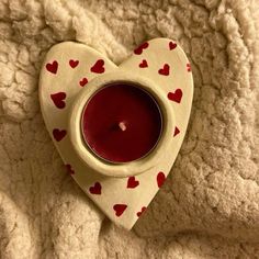 a heart shaped tea light holder with a red candle in it on a white blanket