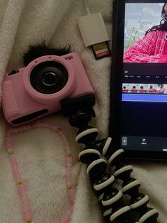 a pink camera sitting on top of a white blanket next to a cell phone and other items