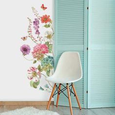 a white chair sitting in front of a wall with flowers painted on it and a blue door