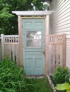 a green door sitting next to a lush green yard with lots of trees and bushes