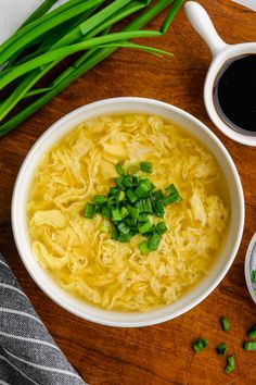 a bowl of noodles and green onions on a wooden table next to two cups of coffee