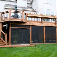 a large wooden deck in front of a white building with green grass and flowers on the balconies