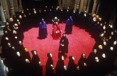 a group of people standing in front of a red circle surrounded by black heads and masks