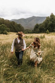 A bride and groom hold hands and smile at each other while walking through an overgrown field with the Great Smoky Mountains behind them on their elopement day Smoky Mountain Couple Photos, Smoky Mountains Elopement, East Tennessee Elopement, Gatlinburg Elopement Photography, Casual Mountain Elopement, Asheville Nc Elopement, Elopement Ideas Tennessee, Gatlinburg Tennessee Elopement, Great Smoky Mountains Wedding