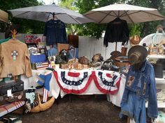 an outdoor flea market with hats, clothing and other items on display under umbrellas