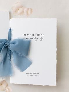 a wedding card with a blue ribbon tied to the front and back of it, next to flowers