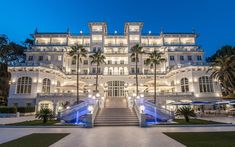 a large white building with lots of windows and palm trees in front of it at night