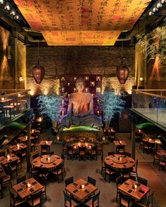 a buddha statue sitting in the middle of a restaurant with many tables and chairs around it