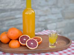 oranges and grapefruit on a wooden tray next to a bottle