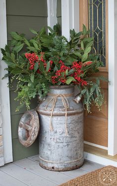 a large metal container with red berries and greenery in it sitting on the front porch