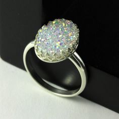 This stunning and sparkly ring includes white natural Druzy Quartz gemstone set on Sterling Silver oval bezel mounting. RING DESCRIPTION: ♦ RING MATERIAL: Sterling Silver ♦ GEMSTONE: Natural Druzy Quartz ♦ STONE COLOR: White ♦ STONE GRADE: A ♦ STONE SHAPE: Oval ♦ STONE DIMENSION: 14x10 mm The ring comes in a nice gift box as featured in the picture #5. It is ready for gift giving! ☛Please select your desired ring size from Size dropdown when ordering☚ View all of my Druzy rings: ► http://www.ets Sparkling White Crystal Ring For Wedding, White Crystal Promise Ring With Stone Setting, White Crystal Birthstone Ring With Round Stone, Adjustable White Rings With Stones, Dazzling White Cluster Ring Gift, White Promise Ring With Stone Setting, White Gemstone Crystal Promise Ring, White Crystal Gemstone Ring For Promise, White Crystal Ring With Stones For Anniversary