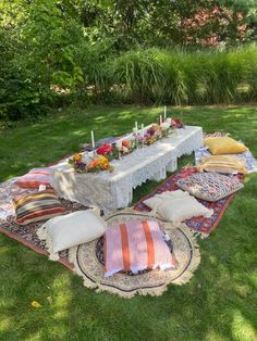 a table with pillows and candles on it in the middle of a grassy area surrounded by trees