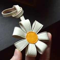 a hand holding a small white flower with yellow center on it's end and a leather strap around the edge