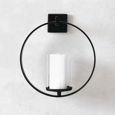 a black candle holder with a white candle in the middle and a circular ring around it