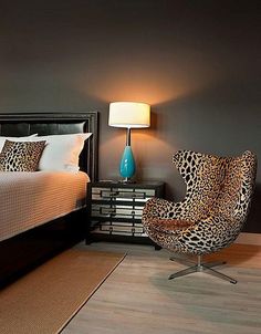 a leopard print chair sits in front of a bed and nightstand with a lamp on it