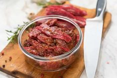 a glass bowl filled with meat sitting on top of a cutting board next to a knife