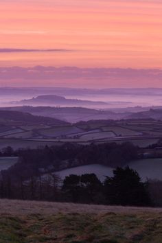 the sun is setting over rolling hills and fields