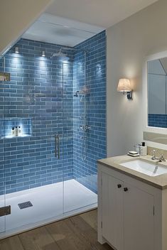 a bathroom with blue tiles on the shower wall and wooden floor, along with a white sink