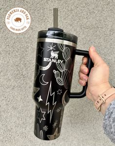 a person holding a black coffee cup with stars and moon designs on it, in front of a gray wall